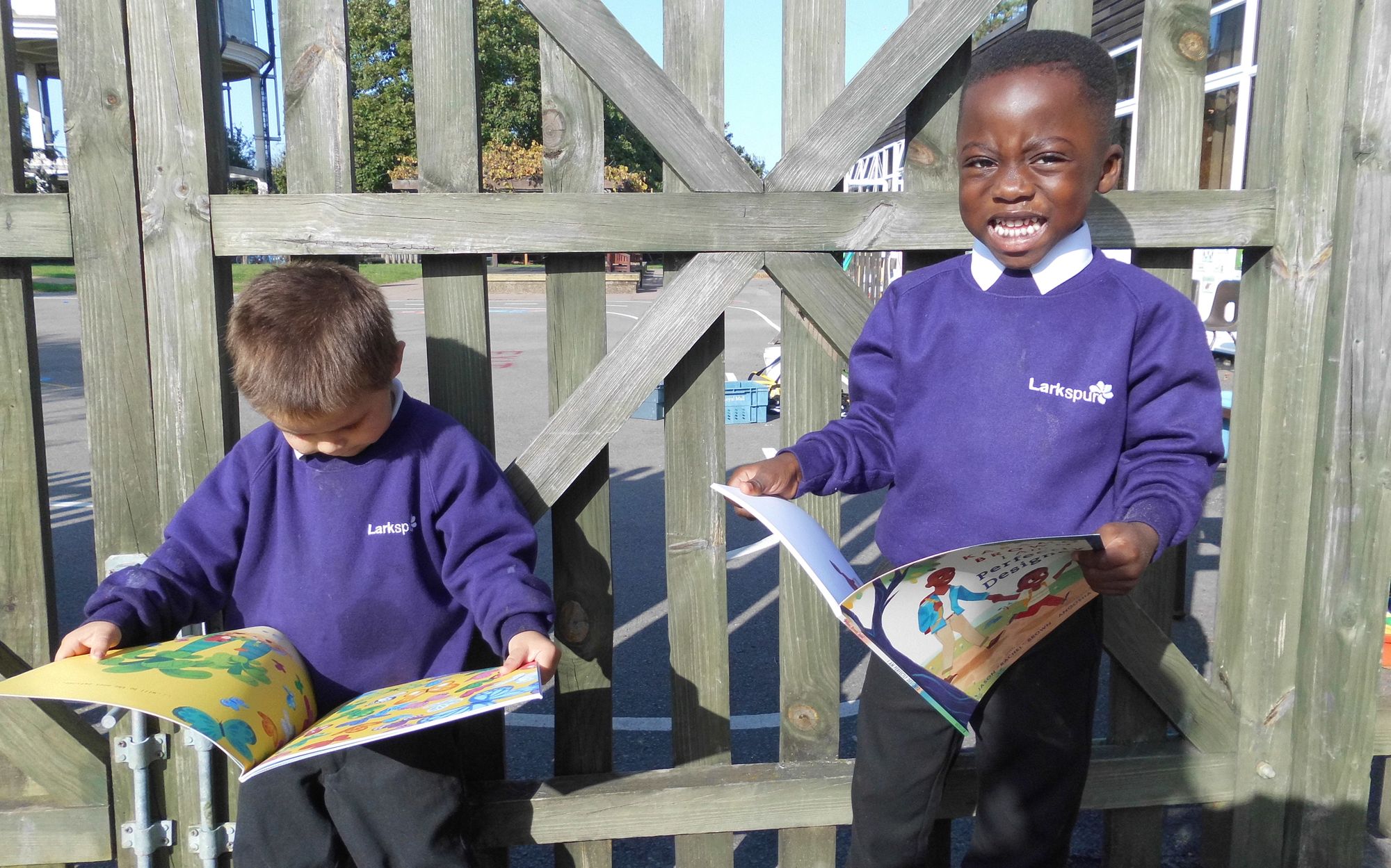 Two young children in purple school uniform stand looking at picture books in front of the camera